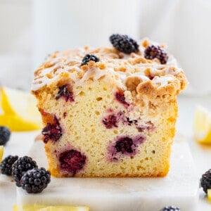 Blackberry Lemon Loaf on a Marble Cutting Board Surrounded by Blackberries and Lemon.