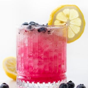 Glass of Spiked Blueberry Lemonade that is Backlit and Has a Lemon Wheel.