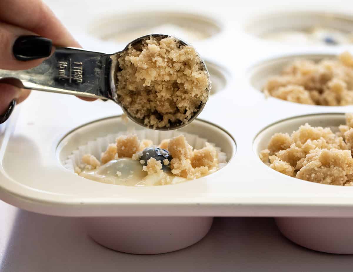 Adding Crumb Topping to Blueberry Lemon Muffin Batter in a Pan.