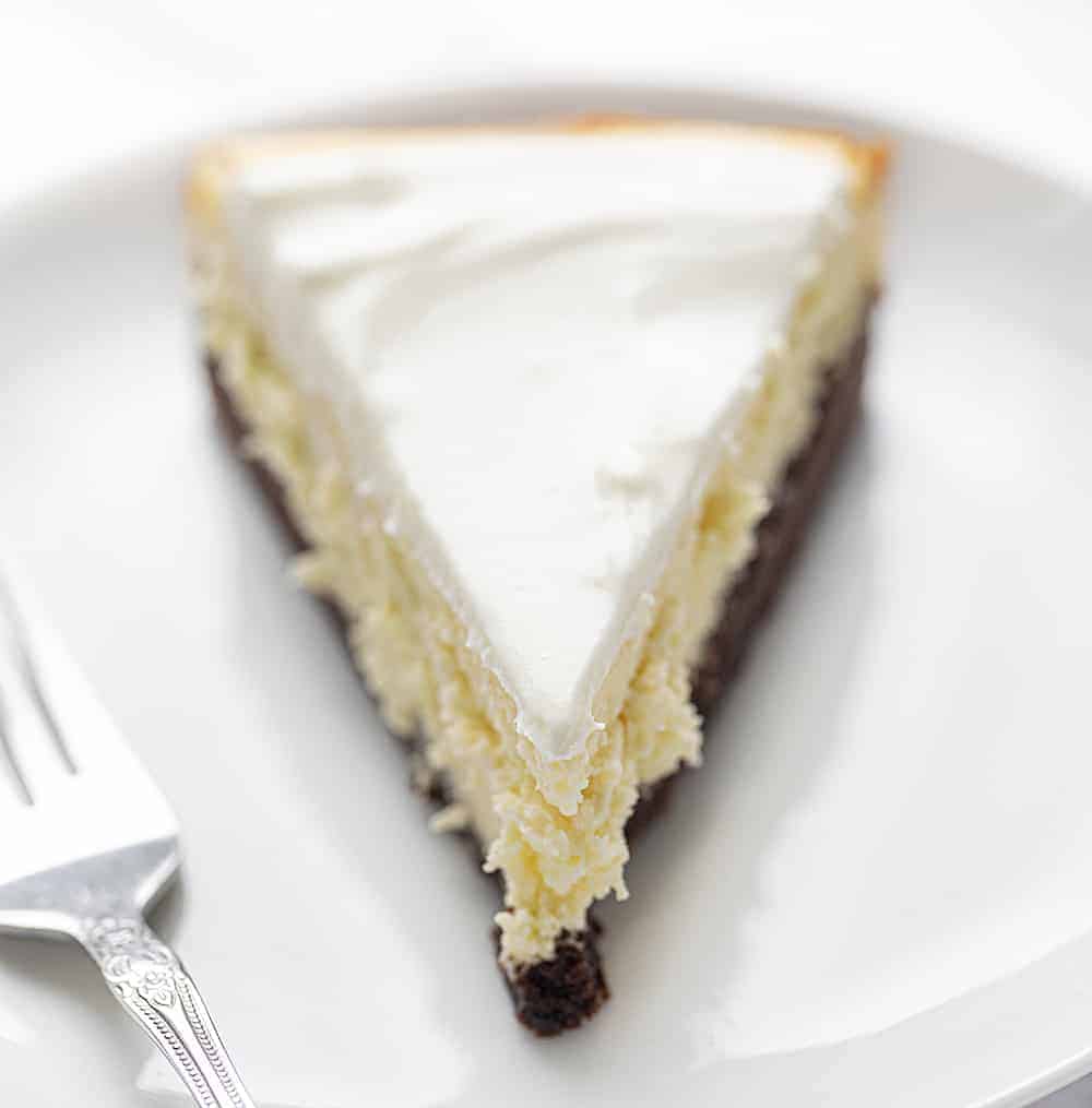 One PIece of Brownie Bottom Cheesecake on White Plate with Fork Next to It