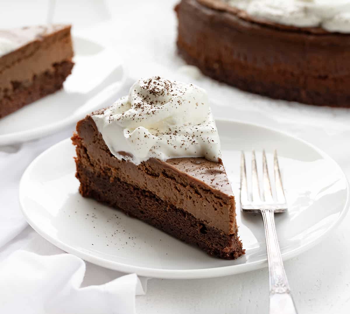 Pieces of Brownie Bottom Chocolate Cheesecake on White Plates with Form.