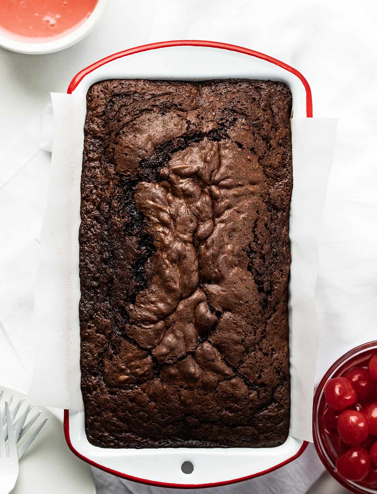 Loaf of Cherry Brownie Bread in a White Pan with Red Rim on a White Counter.