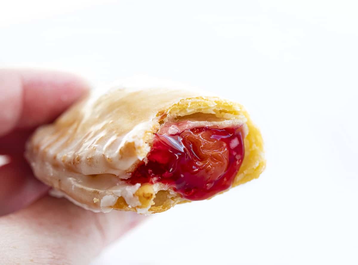 Hand Holding Cherry Hand Pie Showing the Inside. Dessert, Snack, Hand Pies, Fried Pies, Fried Hand Pies, Cherry Pies, Air Fryer Cherry Hand Pies, Fried Cherry Hand Pies, Oven Cherry Hand Pies, Cherry Desserts, Baking, Cherry Recipes, Christmas Recipes, Summer Desserts, i am baker, iambaker