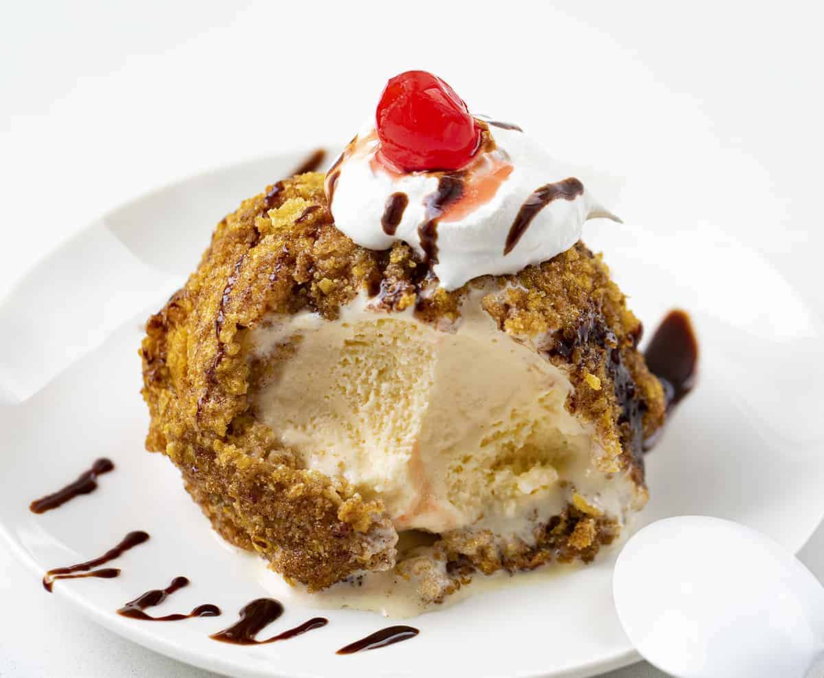 Scoop of Fried Ice Cream on a Plate with Bites Removed and its Drizzled in Hot Fudge.