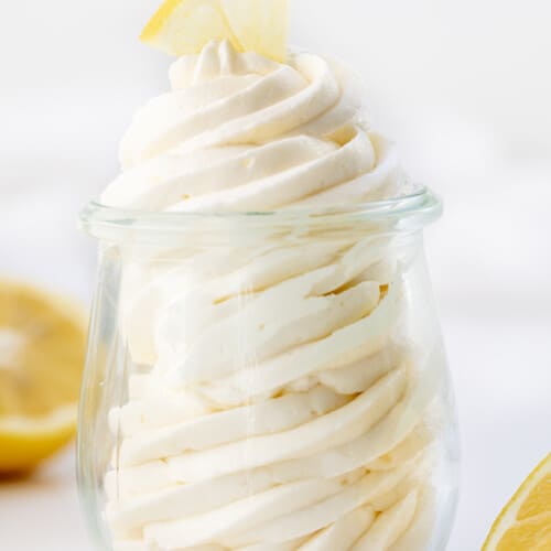 Lemon Ermine Frosting Piped into a Glass Jar with Lemons around it.