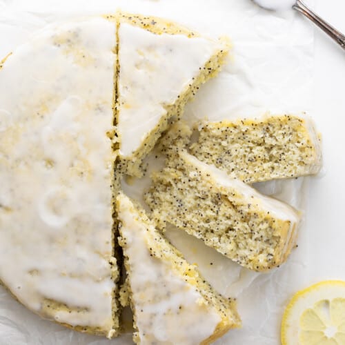 Whole Lemon Poppy Seed Cake on a White Piece of parchment Paper with Four Pieces Cut and Two Pieces on Their Sides Showing Tender Crumb.