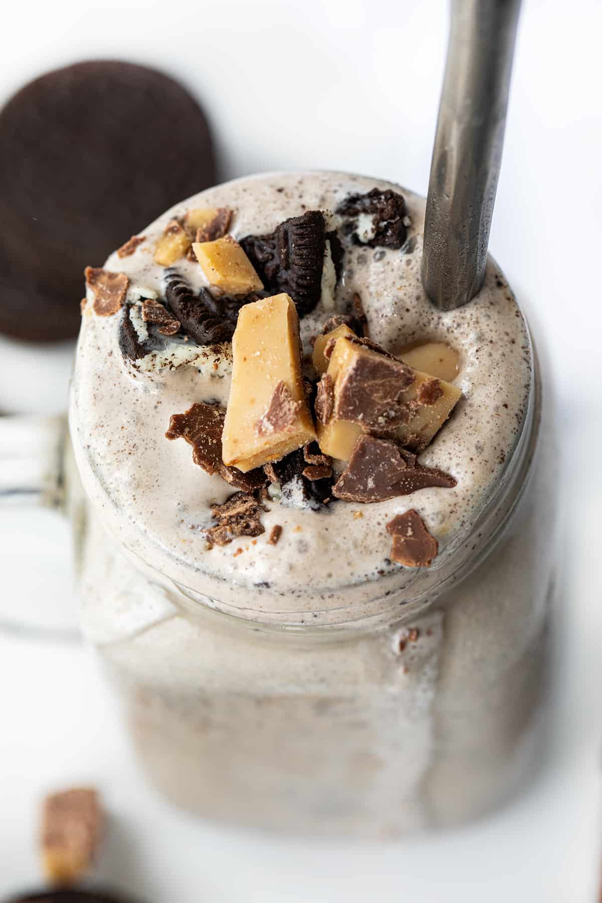 Mug of Oreo Heath Blizzard, a Recipe Adaptation Based on Dairy Queens Blizzard, and Surrounded by Oreos and Heath.