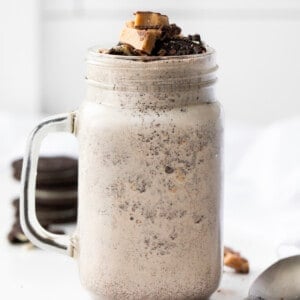 Mug of Oreo Heath Blizzard, a Recipe Adaptation Based on Dairy Queens Blizzard, and Surrounded by Oreos and Heath.